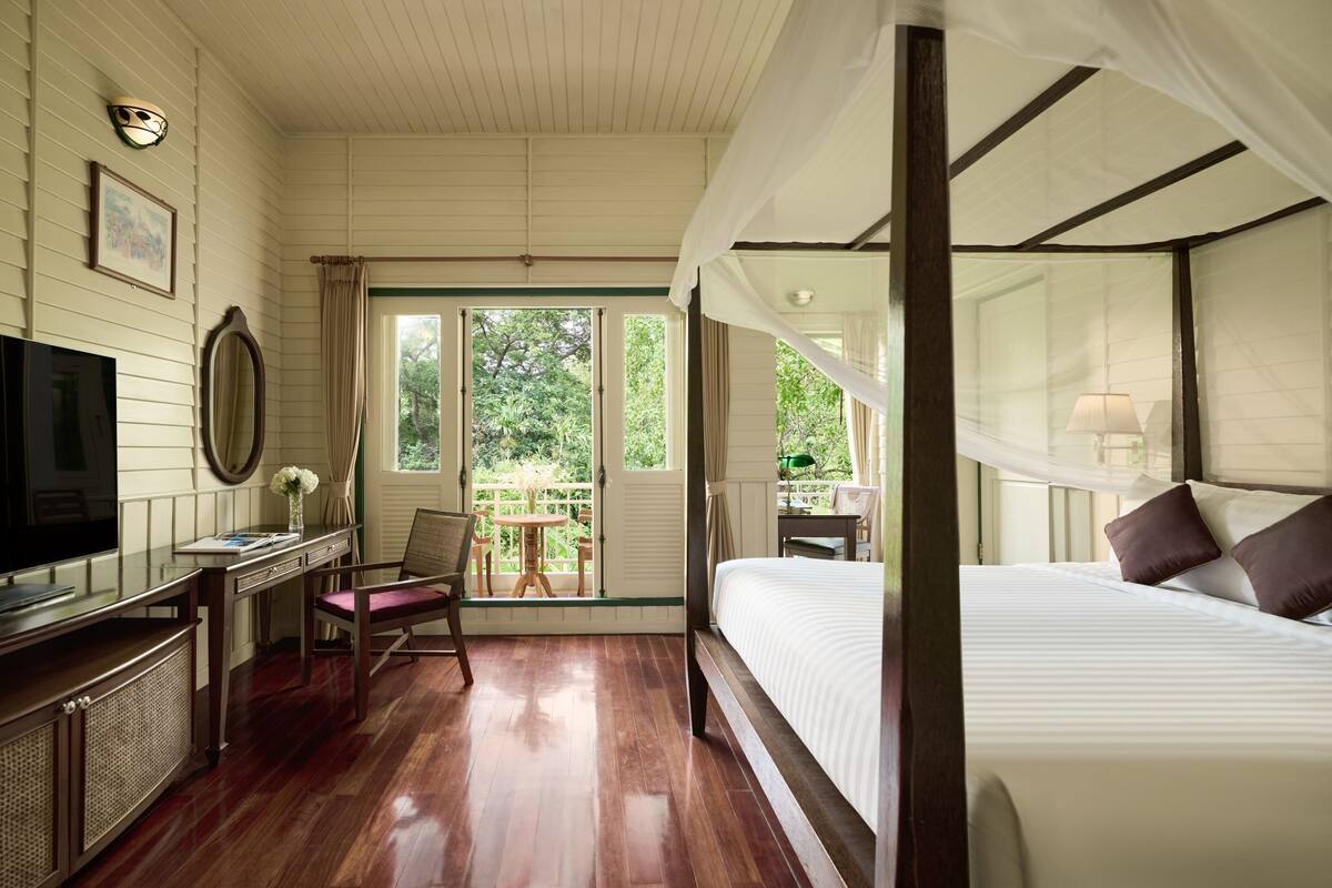 Un dormitorio con cama a dosel, televisor, escritorio con silla y vistas a zonas verdes.