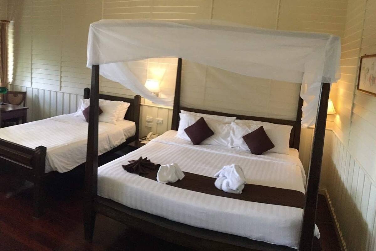 Una habitación con dos camas, cada una con dosel, sábanas blancas y almohadas marrones. Hay lámparas de noche y un teléfono en la mesita de noche.