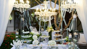 Een feestelijk gedekte tafel met meerdere lagen eten, kaarsen en decoratief glaswerk, voor een achtergrond van groen en witte draperieën.
