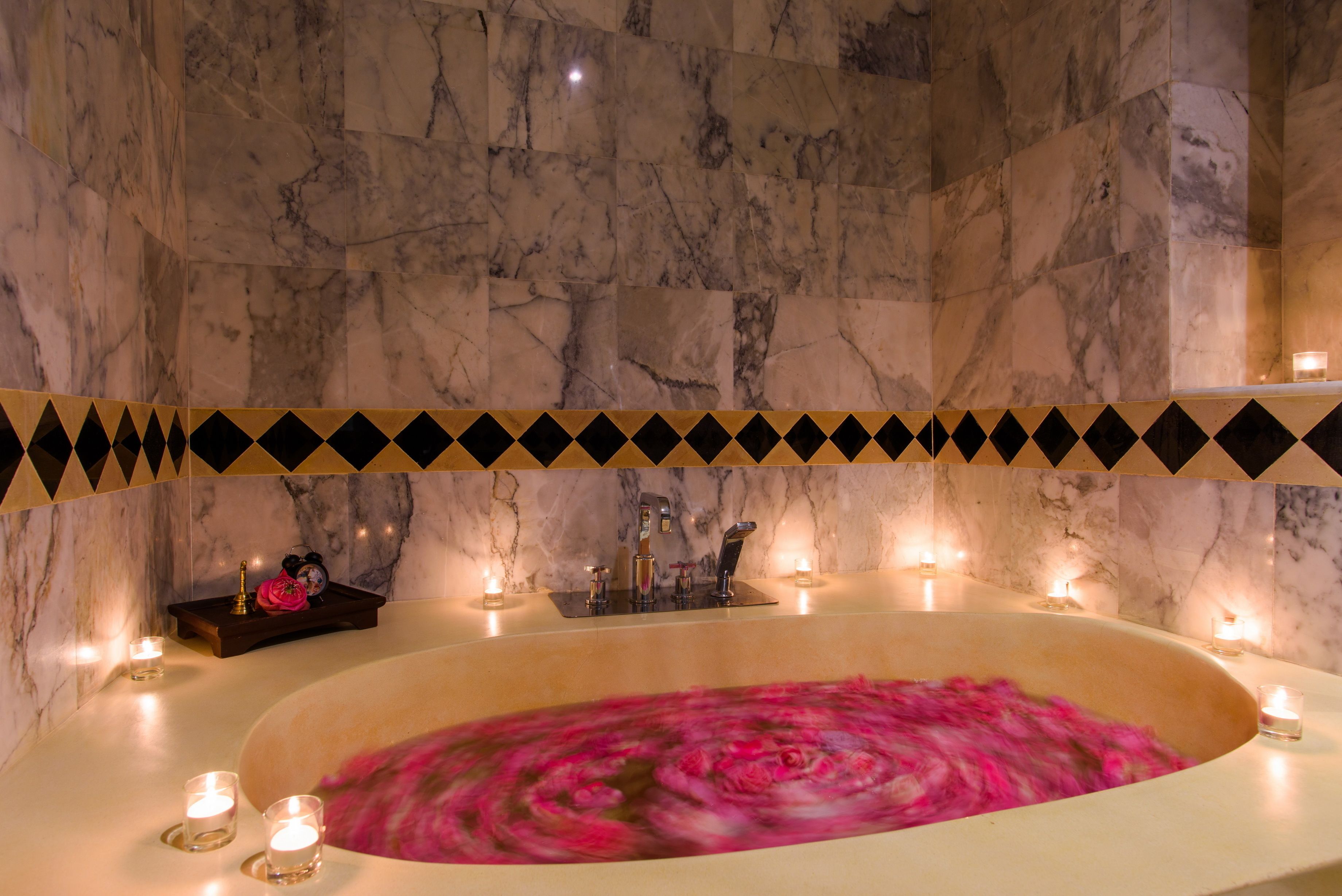 A marble bathroom with a bathtub, candles, and a decorative border.