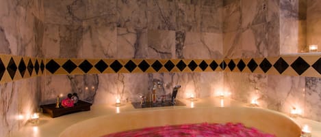 A marble bathroom with a bathtub, candles, and a decorative border.