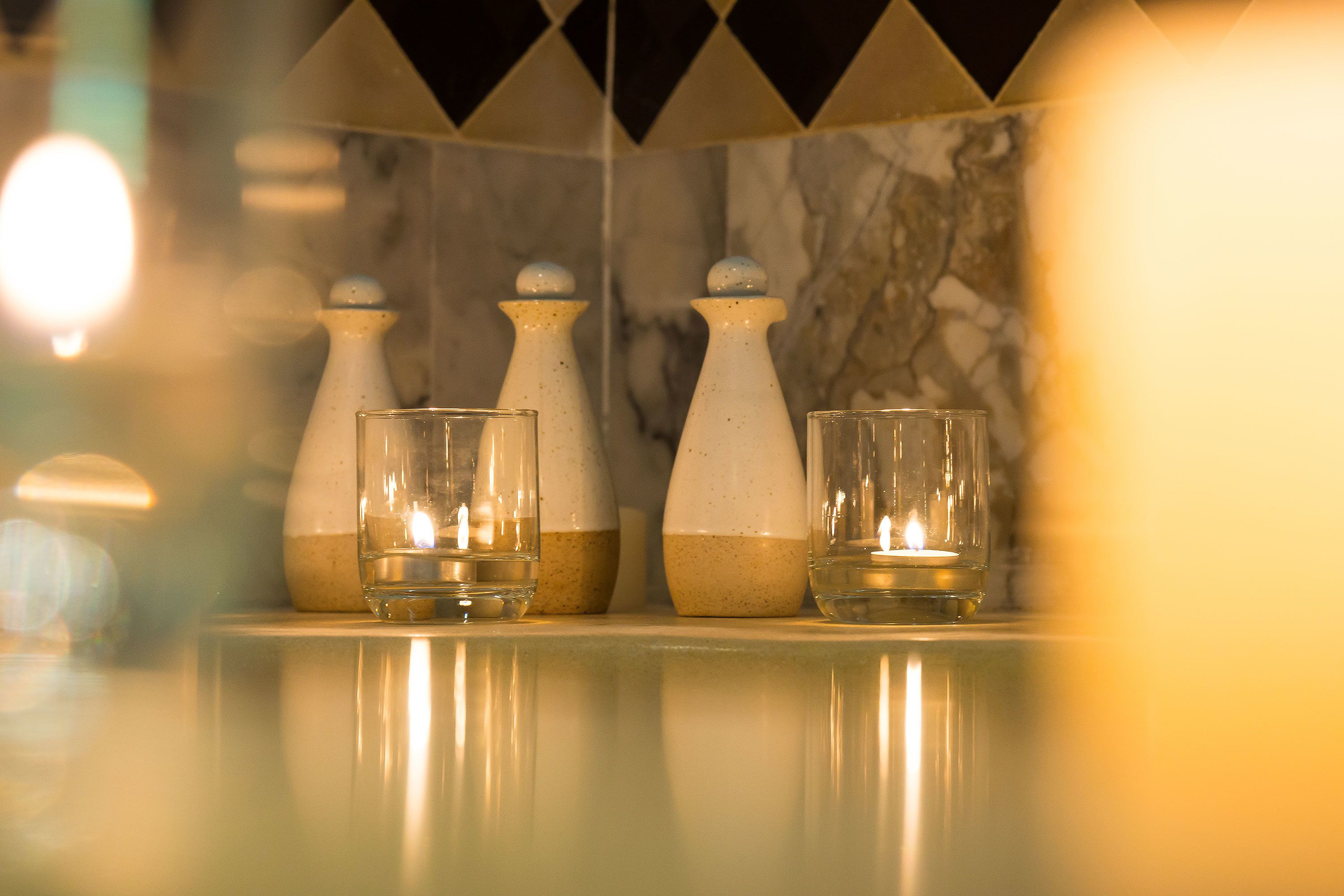 A bathroom with three glass bottles and two glasses on a reflective surface.