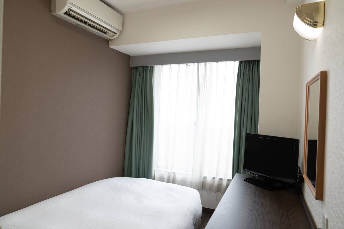 Une chambre d’hôtel avec un lit, un bureau avec une télévision et une fenêtre avec des rideaux.