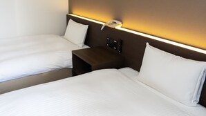 Une chambre d’hôtel avec deux lits, une table de chevet avec un téléphone et un luminaire fixé au mur.