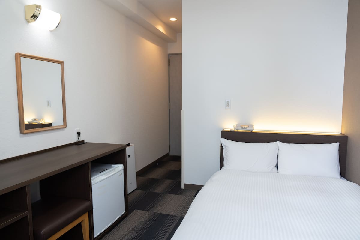 Une chambre d’hôtel comprenant un lit, un bureau avec une chaise, un petit réfrigérateur et un miroir.