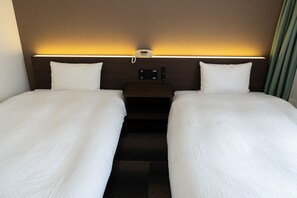 Una habitación de hotel con dos camas, una mesita de noche con lámpara y teléfono.
