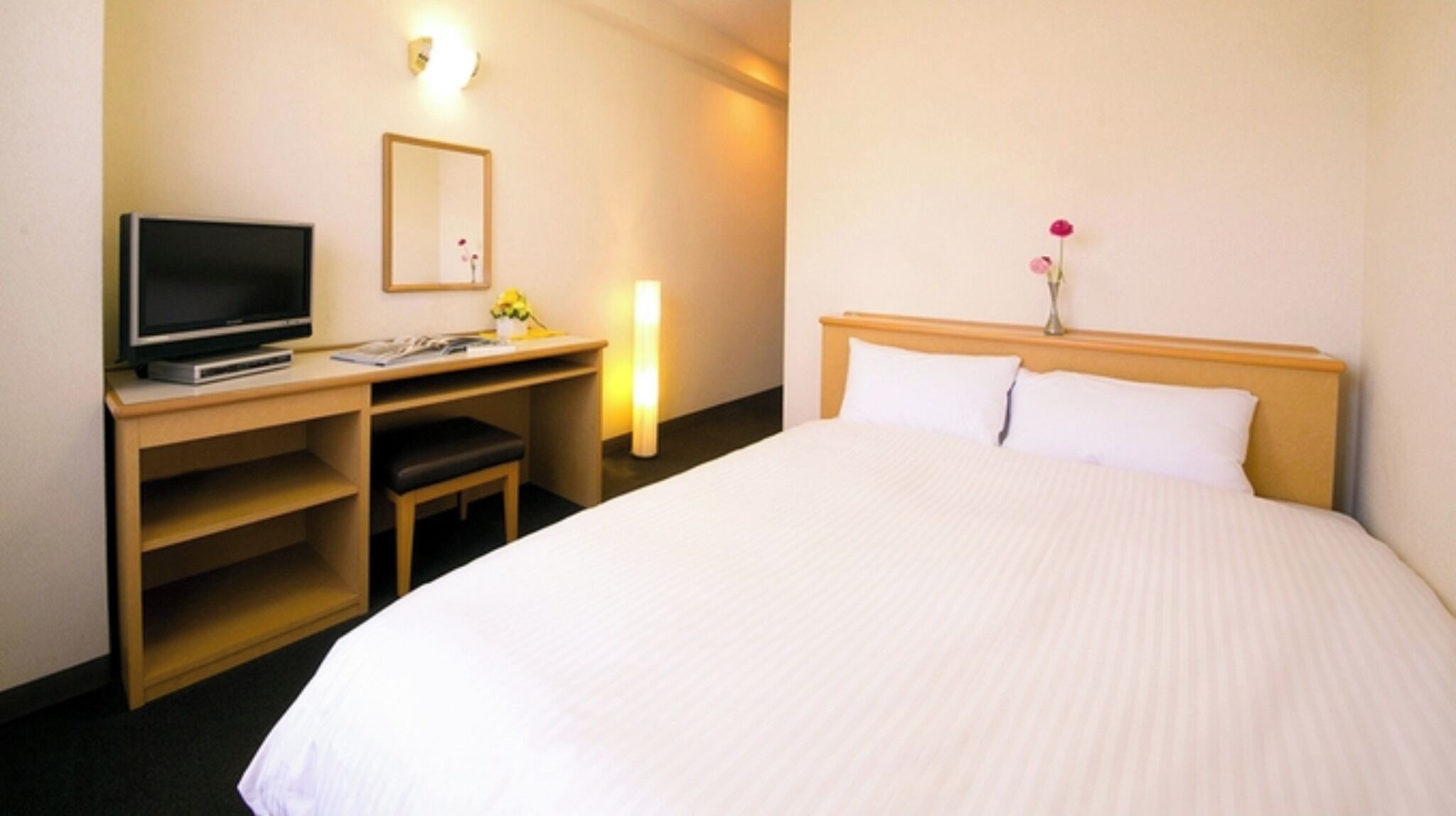 Een hotelkamer met een bed, een bureau met een televisie, een stoel en een nachtkastje met een lamp.