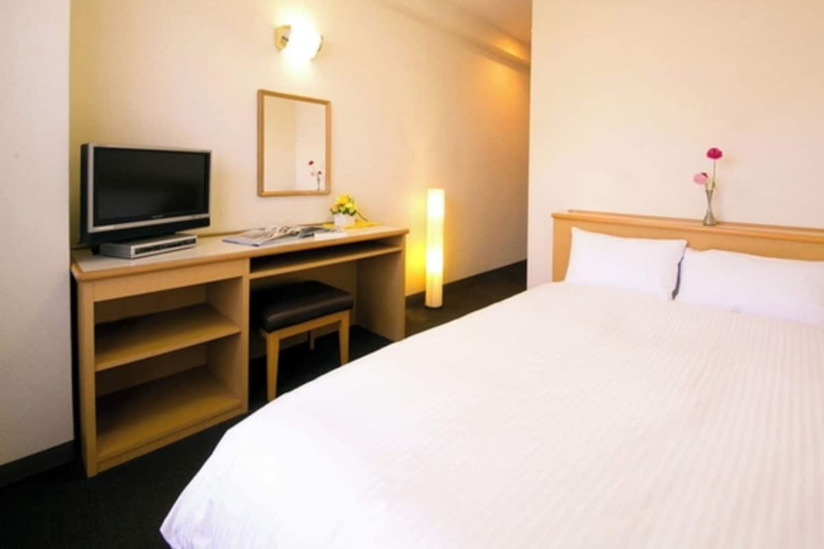 Une chambre d’hôtel comprenant un lit, un bureau avec une télévision, une chaise et une table de chevet avec une lampe.