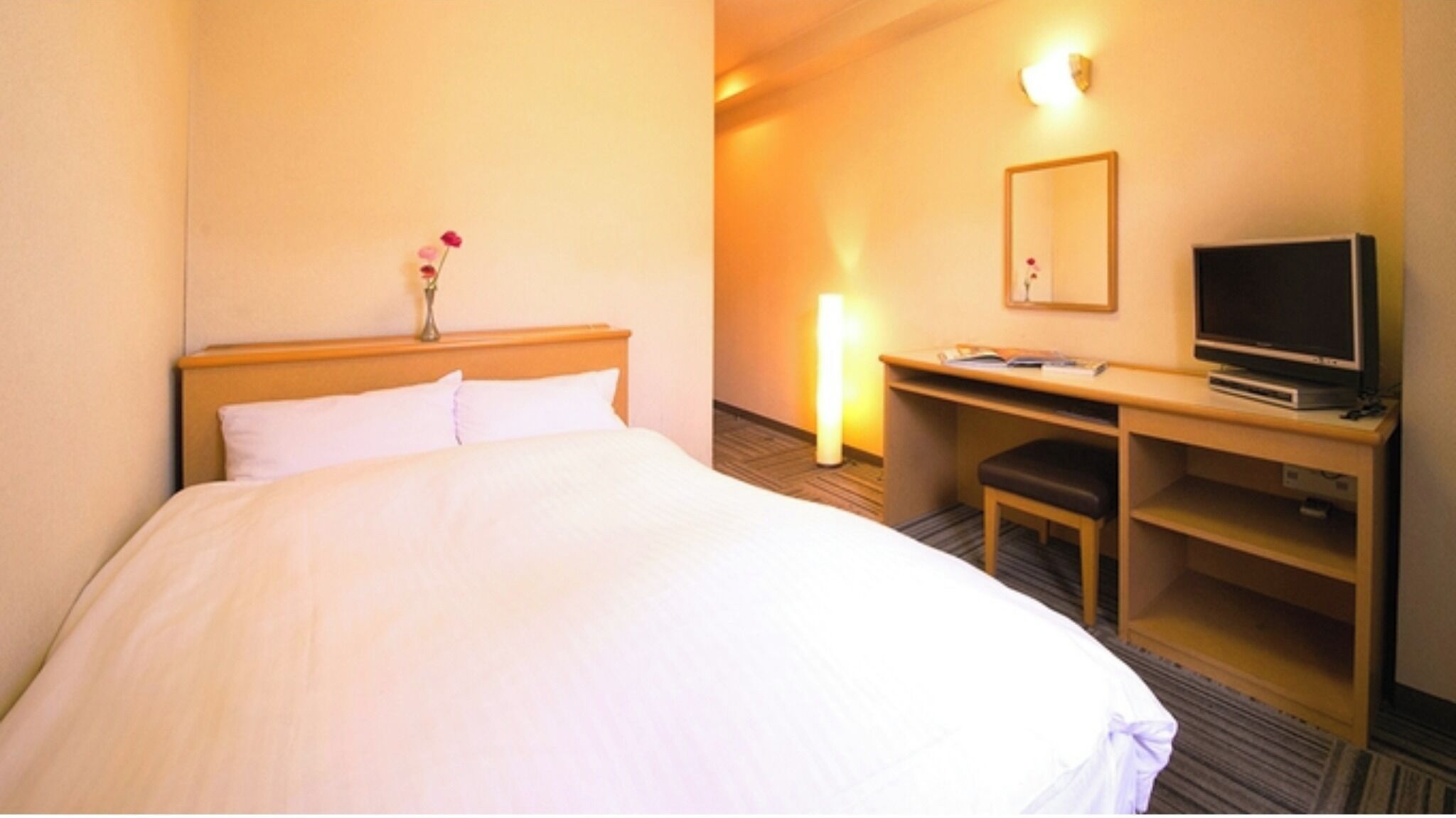 Een hotelkamer met een bed, een bureau met een televisie en een spiegel aan de muur.