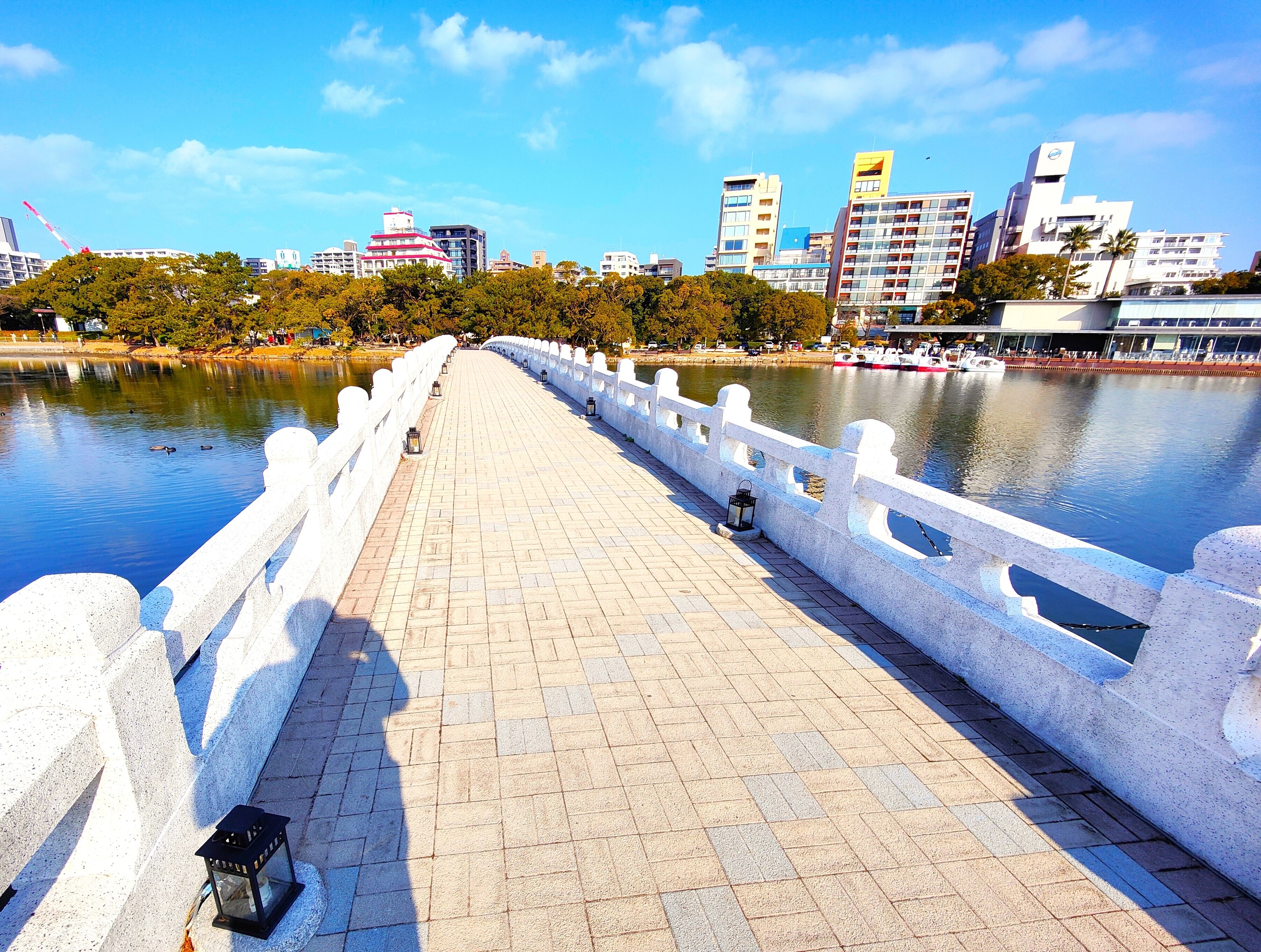 Un puente con barandilla blanca, un camino pavimentado y un río tranquilo.