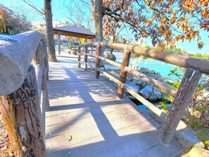 A wooden bridge with a stone railing leading to a wooden pavilion by a body of water.