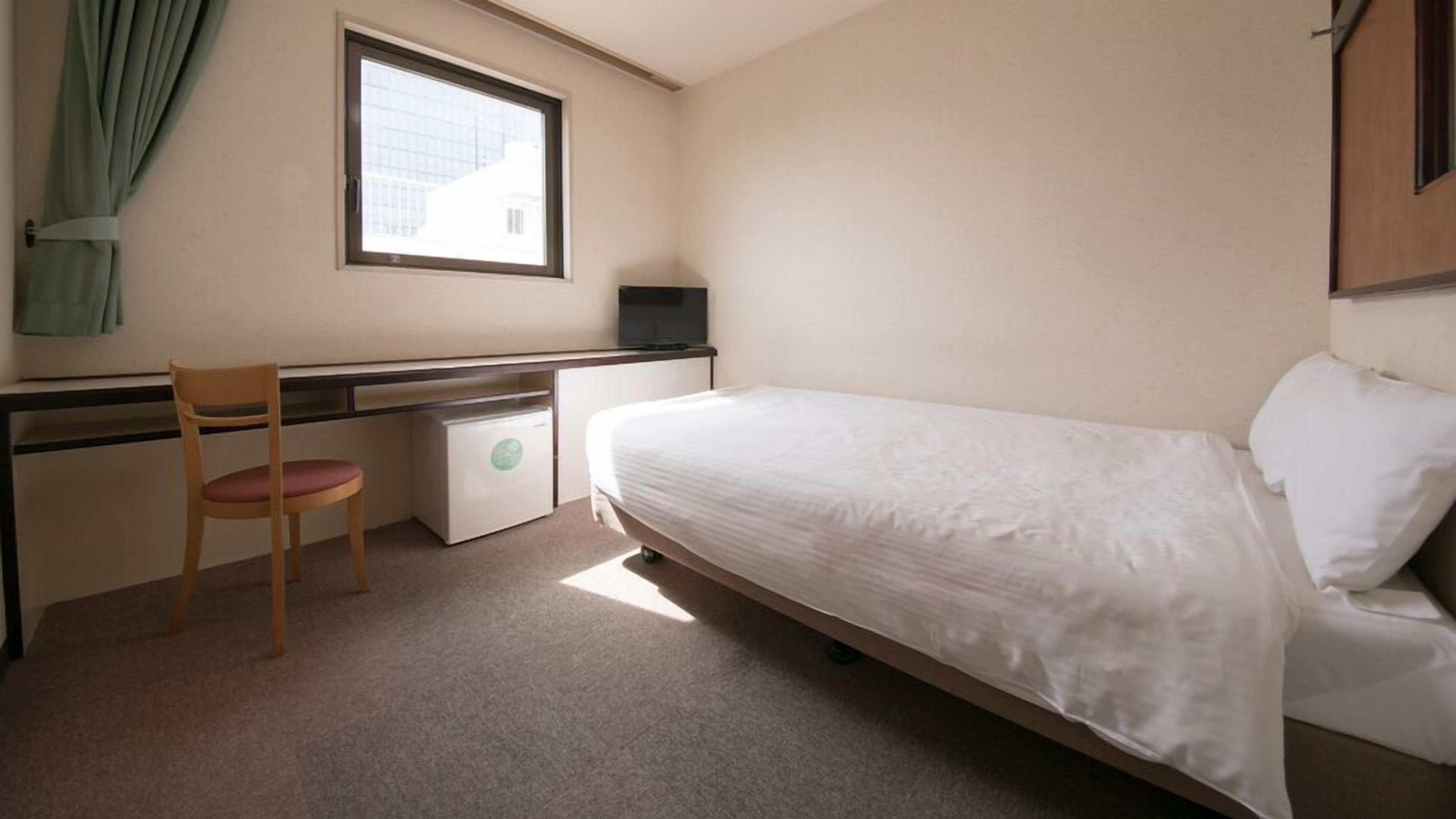 Une petite pièce propre, avec un lit, un bureau, une chaise et une fenêtre.