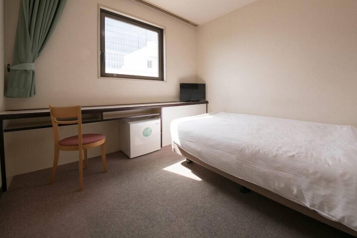 Een kleine, schone kamer met een bed, een bureau, een stoel en een raam.
