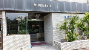 Das äußere Erscheinungsbild des Heiwadai Hotels mit einem deutlichen Eingang, einer Kachelfassade und einer kleinen Gartenanlage mit Pflanzen und Steinen.