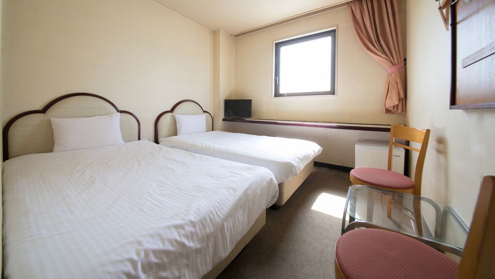 Une chambre avec deux lits, un bureau, une chaise et une fenêtre.