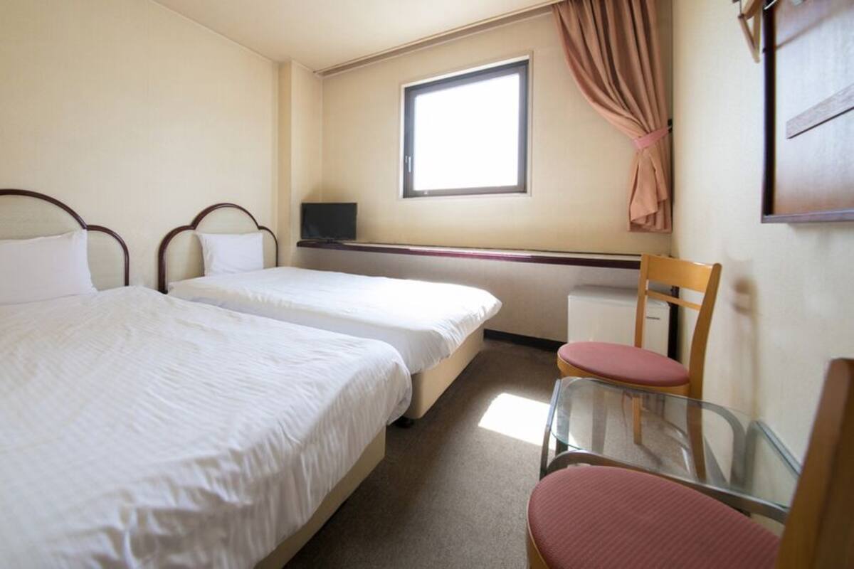 Een kamer met twee bedden, een bureau, een stoel en een raam.