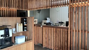 Ein moderner Empfangsbereich mit einer Trennwand aus Holzlatten, einem digitalen Kiosk, einer Kaffeemaschine und einem Schalter mit Registrierkasse.
