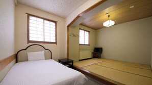 Ein Zimmer mit einem Bett, einem kleinen Tisch, einem Futon, einem Fernseher und einem Fenster mit Blick nach draußen.