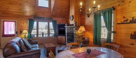 Interior acogedor de una cabaña con chimenea, muebles de madera y vistas al exterior.