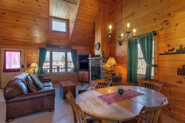 A cozy cabin interior with a fireplace, wooden furniture, and a view of the outdoors. - Rangeley Lake Resort (Rangeley)