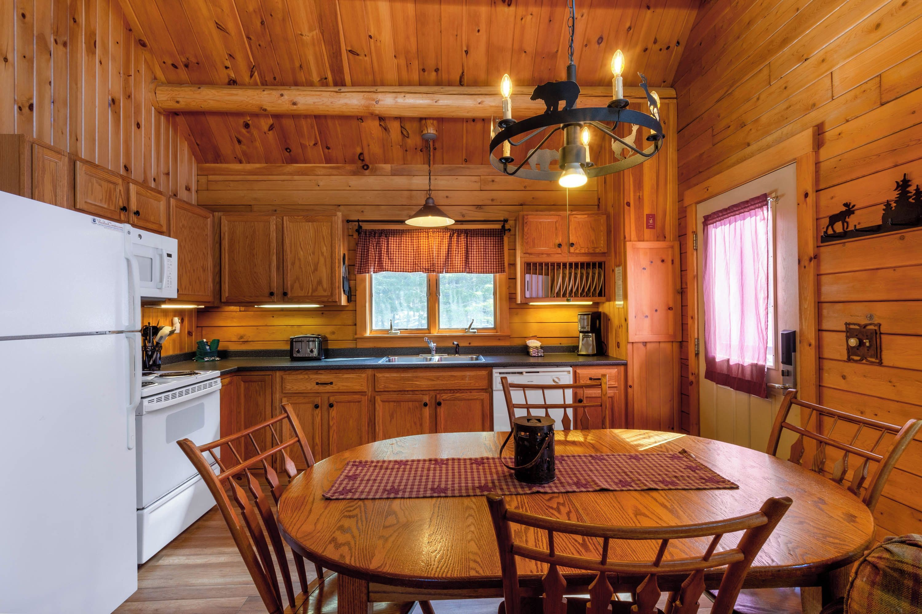 Ein Holzblockhaus-Interieur mit Küche, Essbereich und einer Chandelüster.