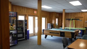 A pool table, a vending machine, and a billiards table in a room with wooden walls and a carpeted floor. - Rangeley Lake Resort (Rangeley)