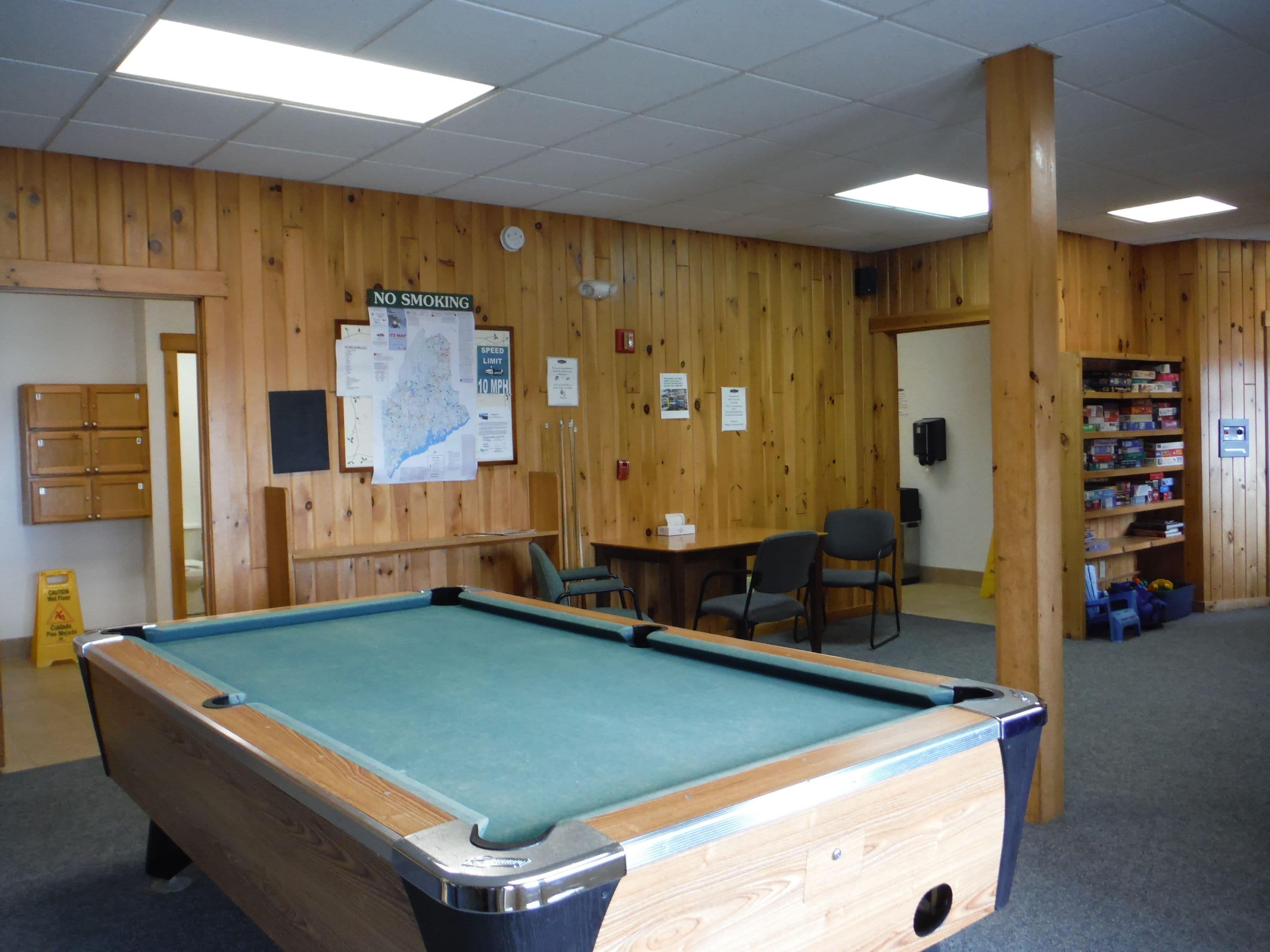A pool table in a room with wooden walls, a map, and a 'No Smoking' sign.