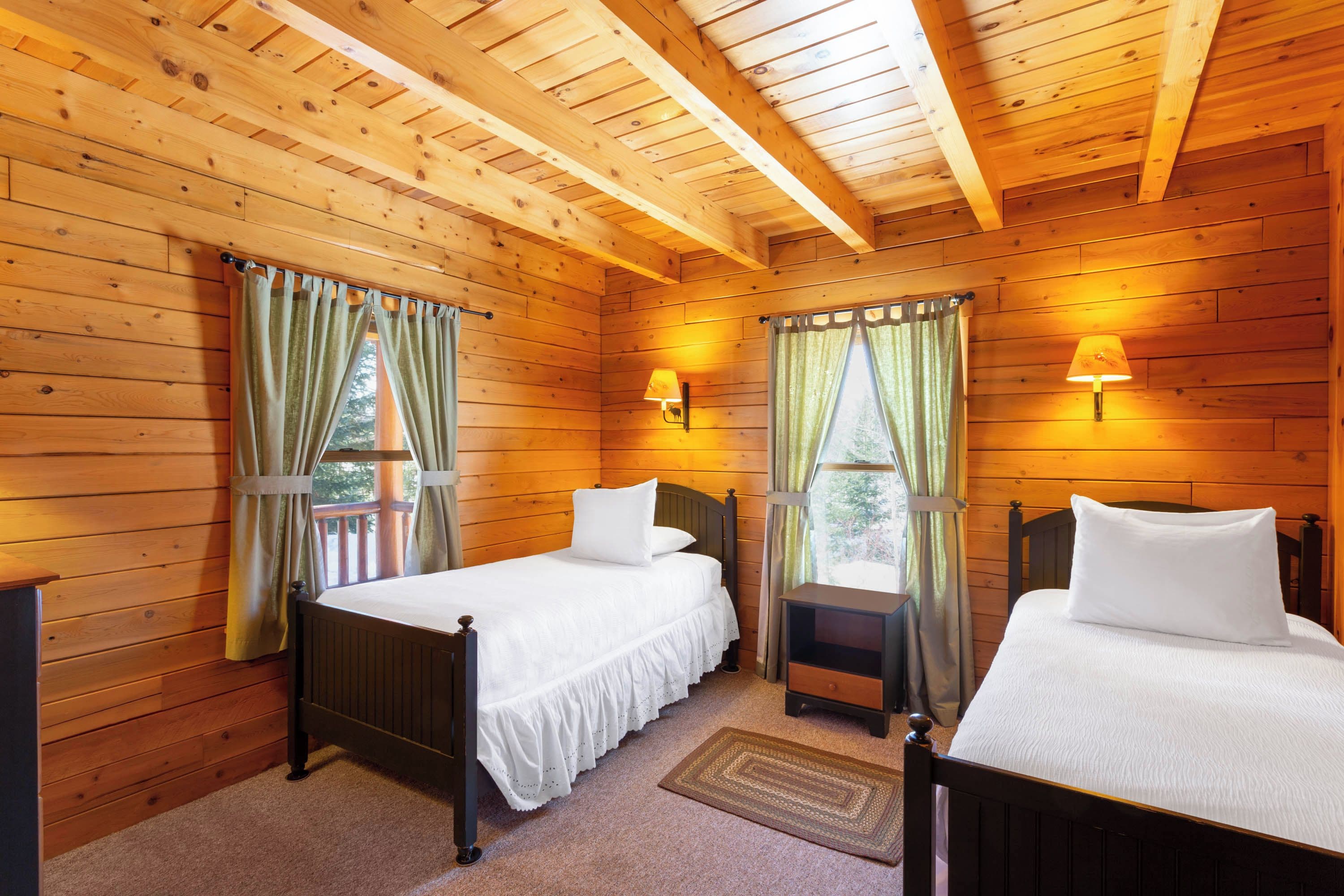 A cabin with two wooden beds, a nightstand, and a window with curtains.