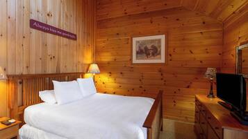 A wooden room with a bed, a nightstand, a lamp, a dresser, and a television.