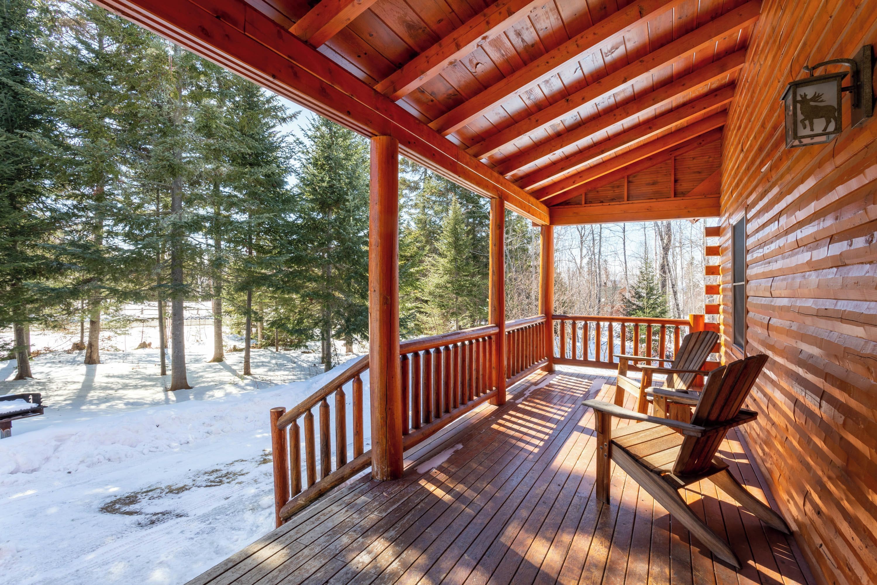A wooden cabin with a covered porch, two chairs, and a bench.