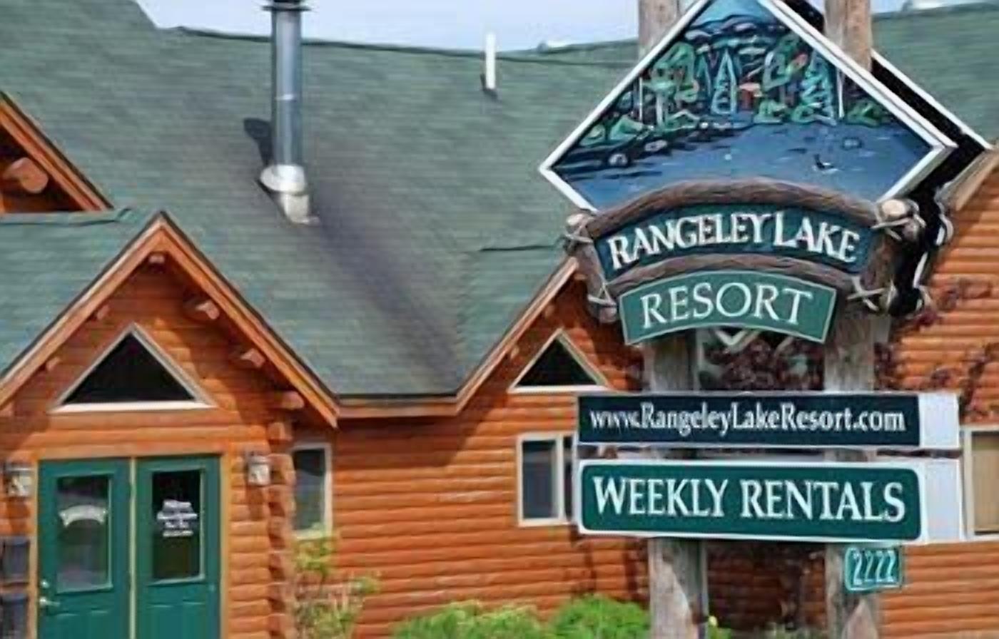 En stuga byggd av trä med en skylt som visar att det är Rangeley Lake Resort och en annan skylt som anger att det finns möjlighet att hyra den per vecka.