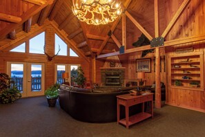 A log cabin interior with a fireplace, leather sofa, and a chandelier.