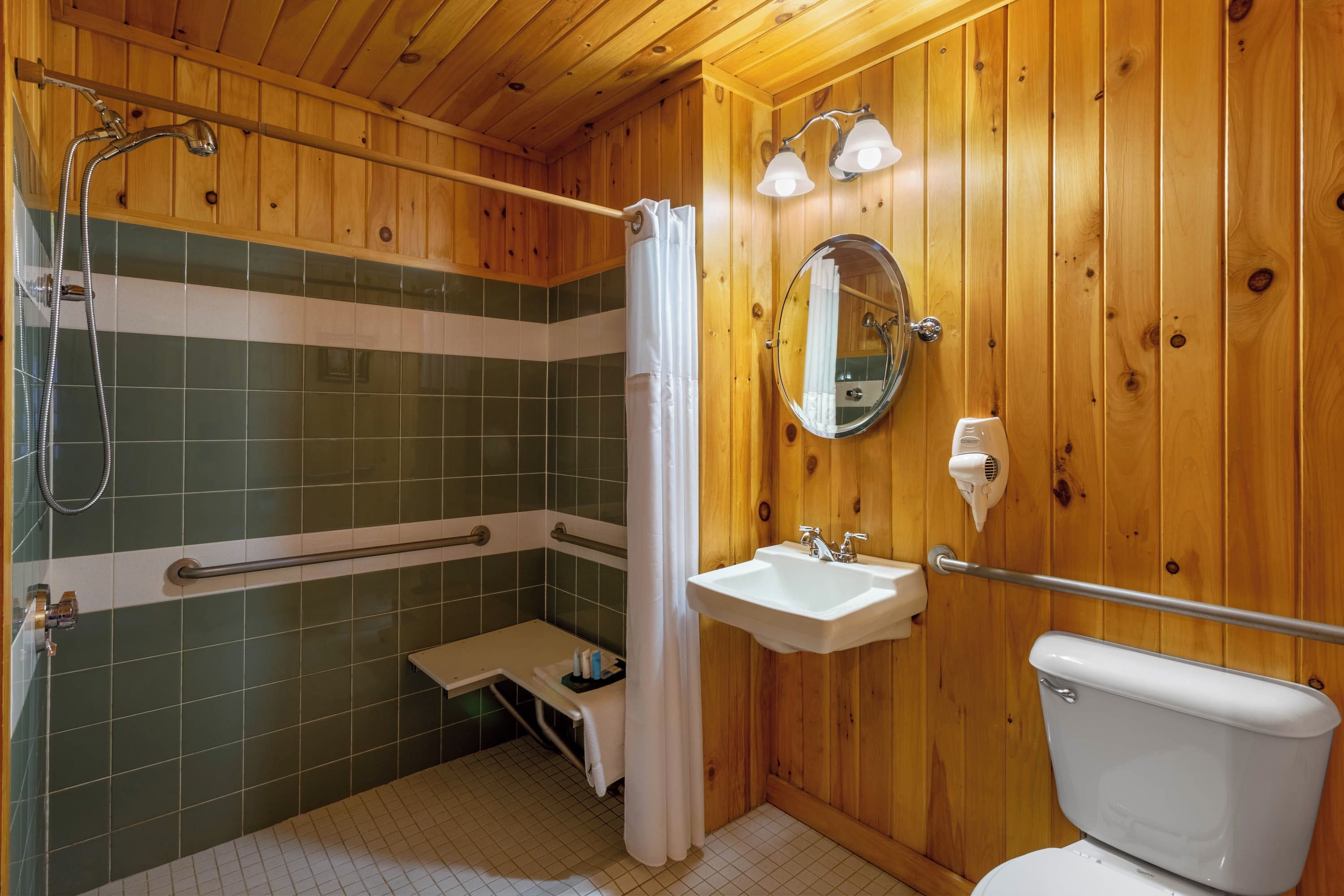 A wooden-paneled bathroom with a shower, a sink, a toilet, and a mirror.