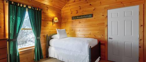 Un dormitorio de cabaña de madera con una cama, una lámpara de pared y una puerta.