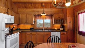 Interior de una cabaña de madera con cocina, comedor y ventana con vistas.