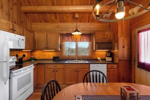 A wooden cabin interior with a kitchen, dining area, and a window with a view. - Rangeley Lake Resort (Rangeley)