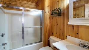 A wooden-paneled bathroom with a glass shower enclosure, a toilet, and a sink with a mirror above it.