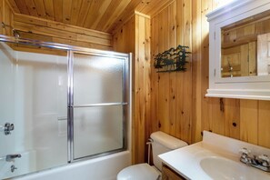 A wooden-paneled bathroom with a glass shower enclosure, a toilet, and a sink with a mirror above it.