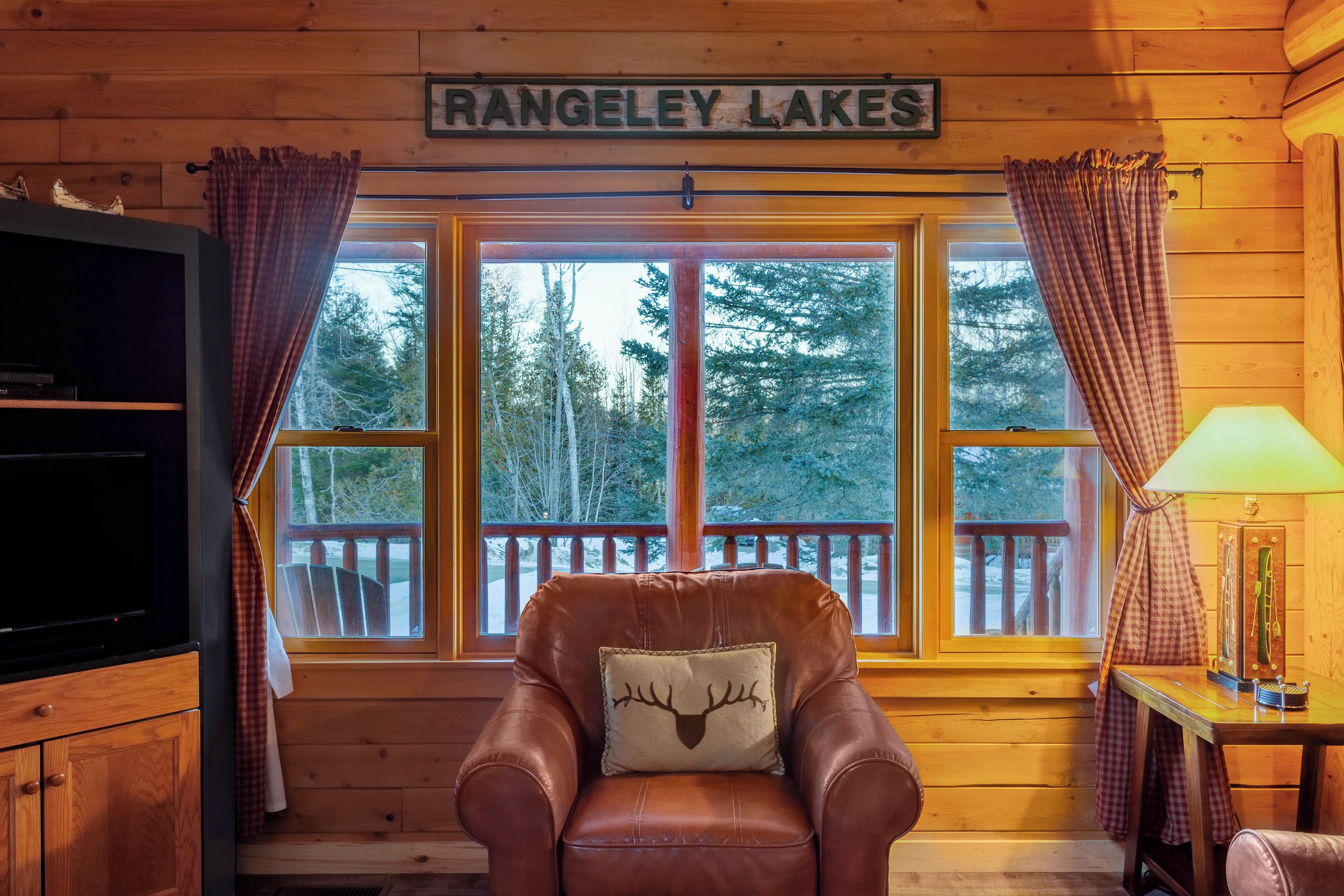 Een interieur van een blokhut met een leren fauteuil, een televisie en een bordje met de tekst 'RANGELEY LAKES'.