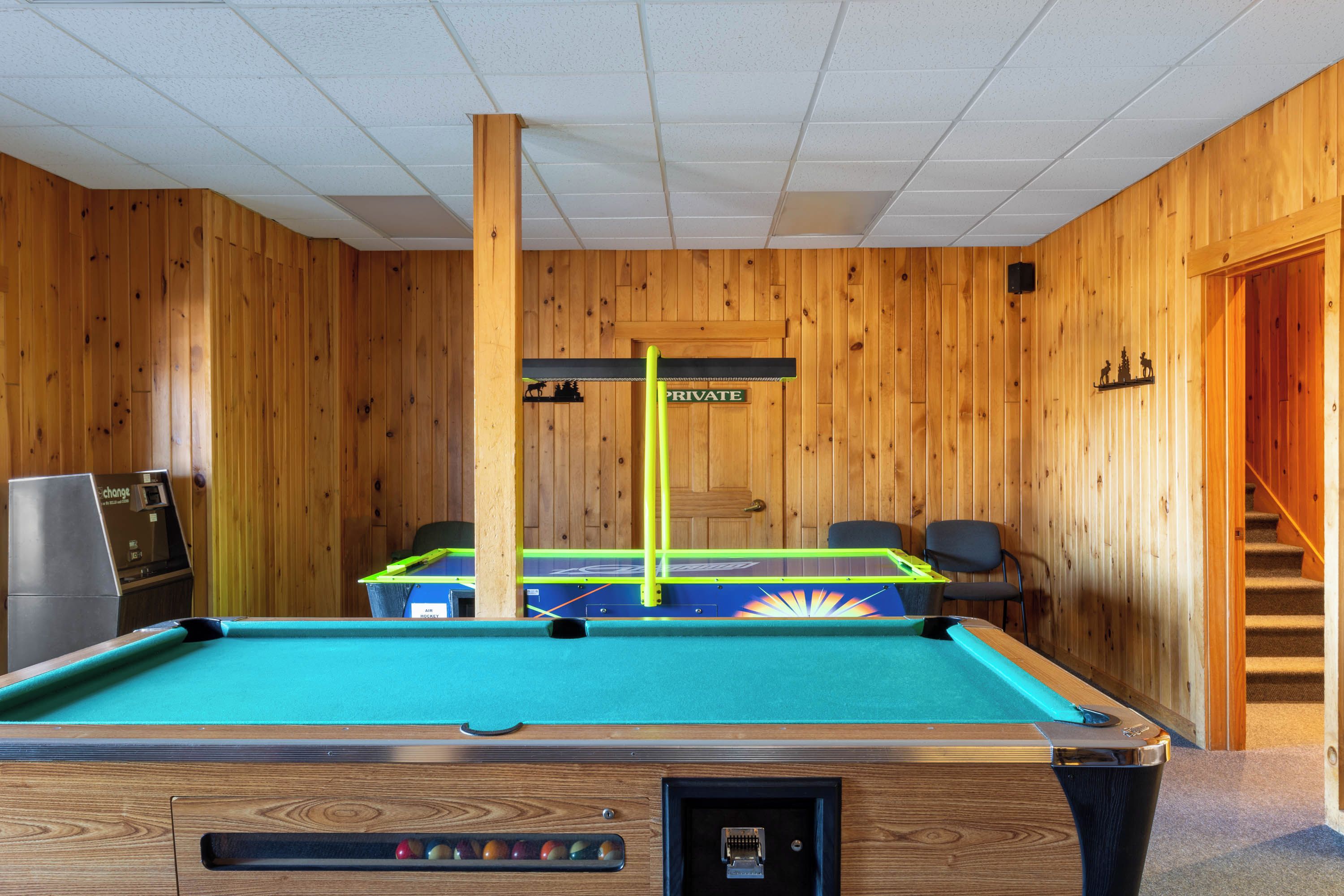 Une table de billard dans une pièce aux murs en bois, avec une porte et un escalier.