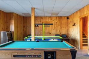 A pool table in a room with wooden walls, a door, and a staircase. - Rangeley Lake Resort (Rangeley)