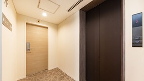 Ein Hotelgang mit einer Holztür mit der Aufschrift 701, einer dunklen Aufzugstür und einem an der Wand montierten Bedienfeld für den Aufzug.