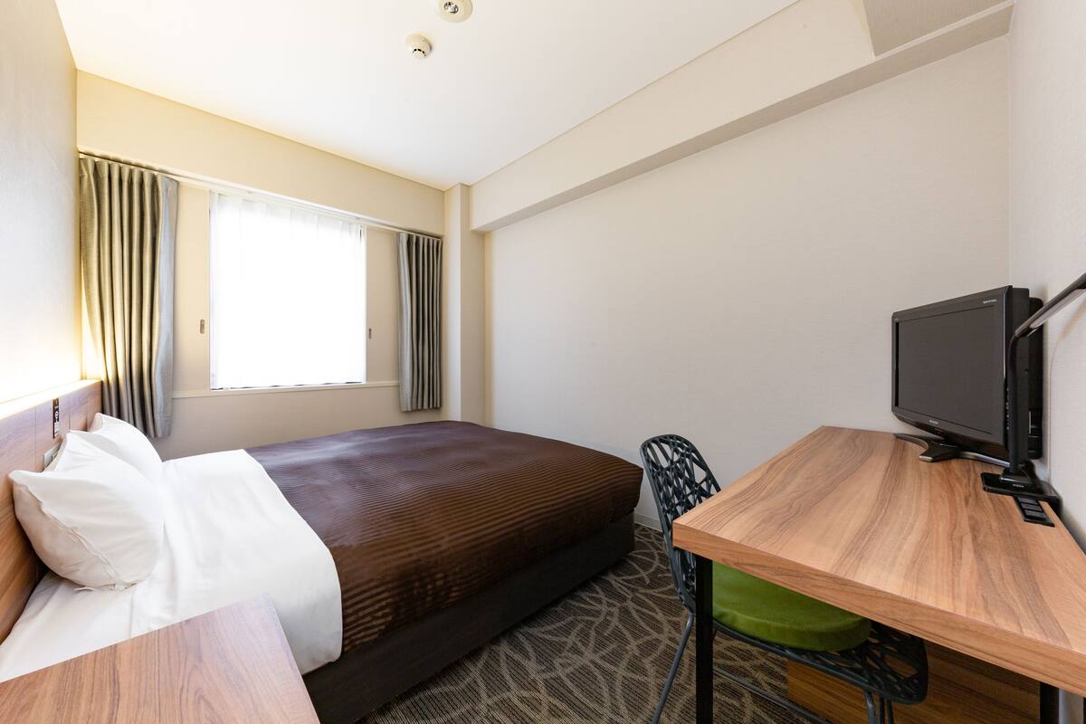 A hotel room with a bed, a desk, a chair, a television, and a window with curtains.