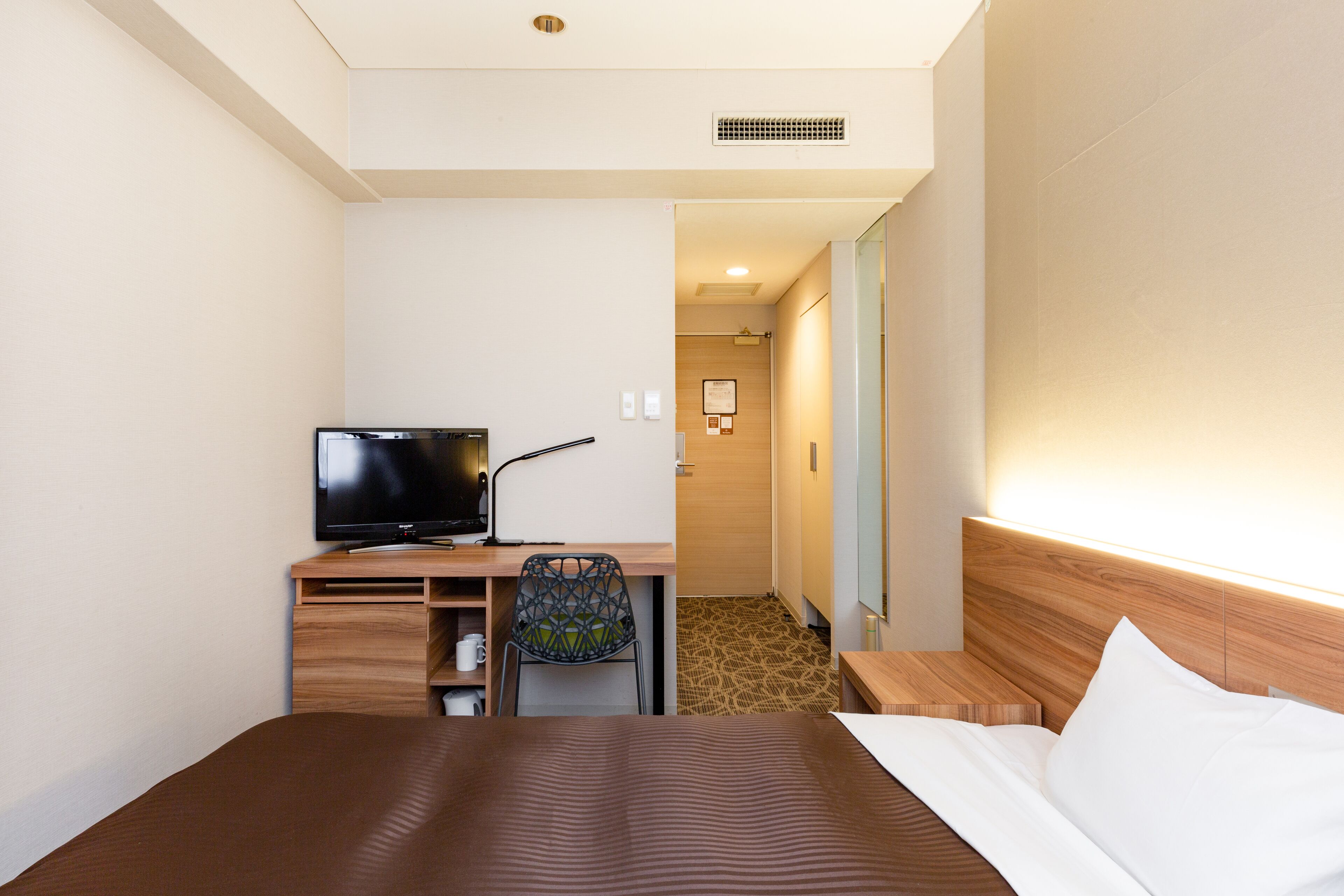 A hotel room with a bed, a desk with a television, a chair, and a small table.