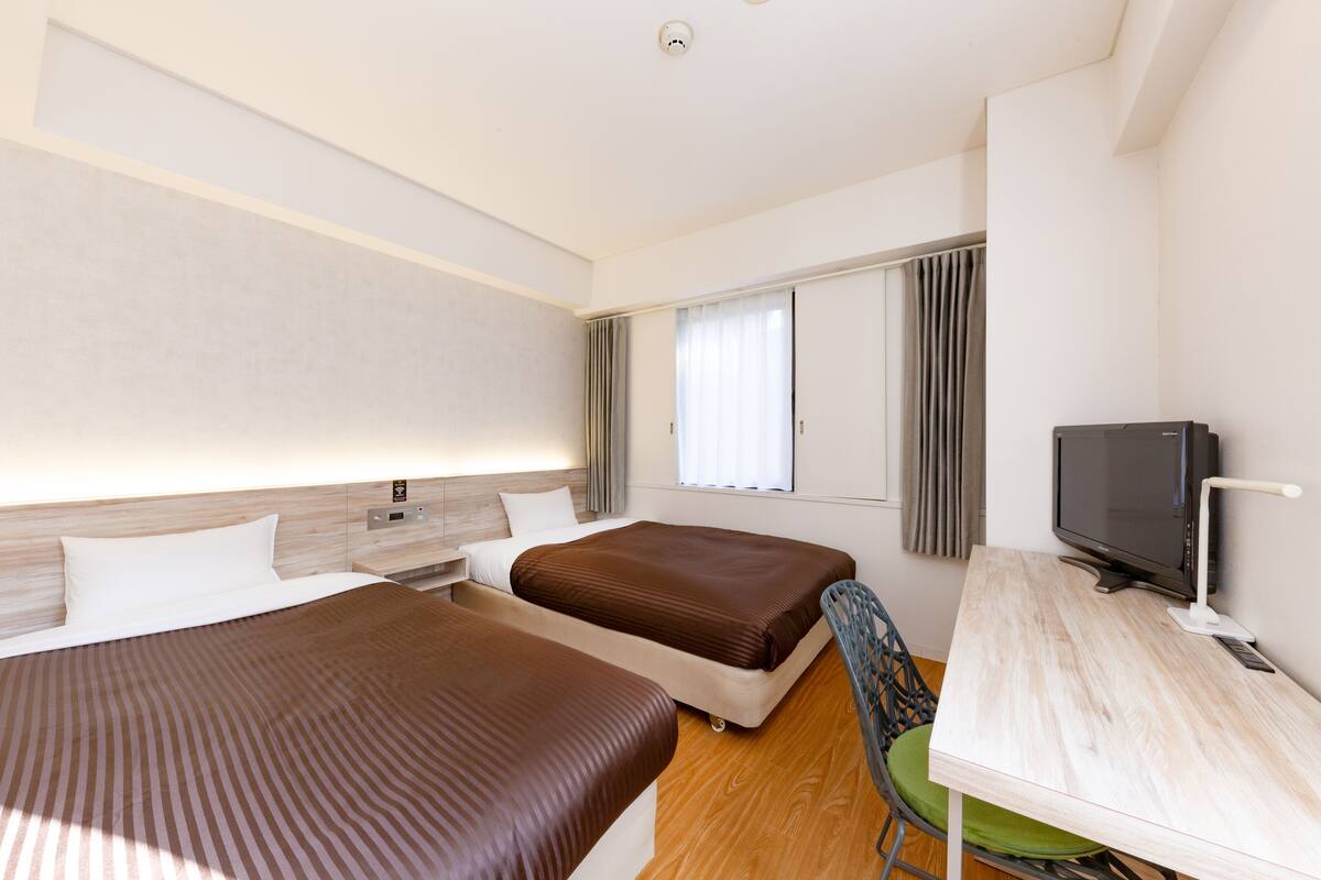 A hotel room with two beds, a desk, a chair, a television, and a window with curtains.