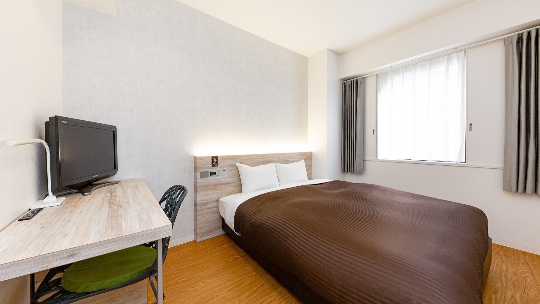 Ein Hotelzimmer mit Bett, Schreibtisch, Fernseher, Stuhl und einem Fenster mit Vorhängen.