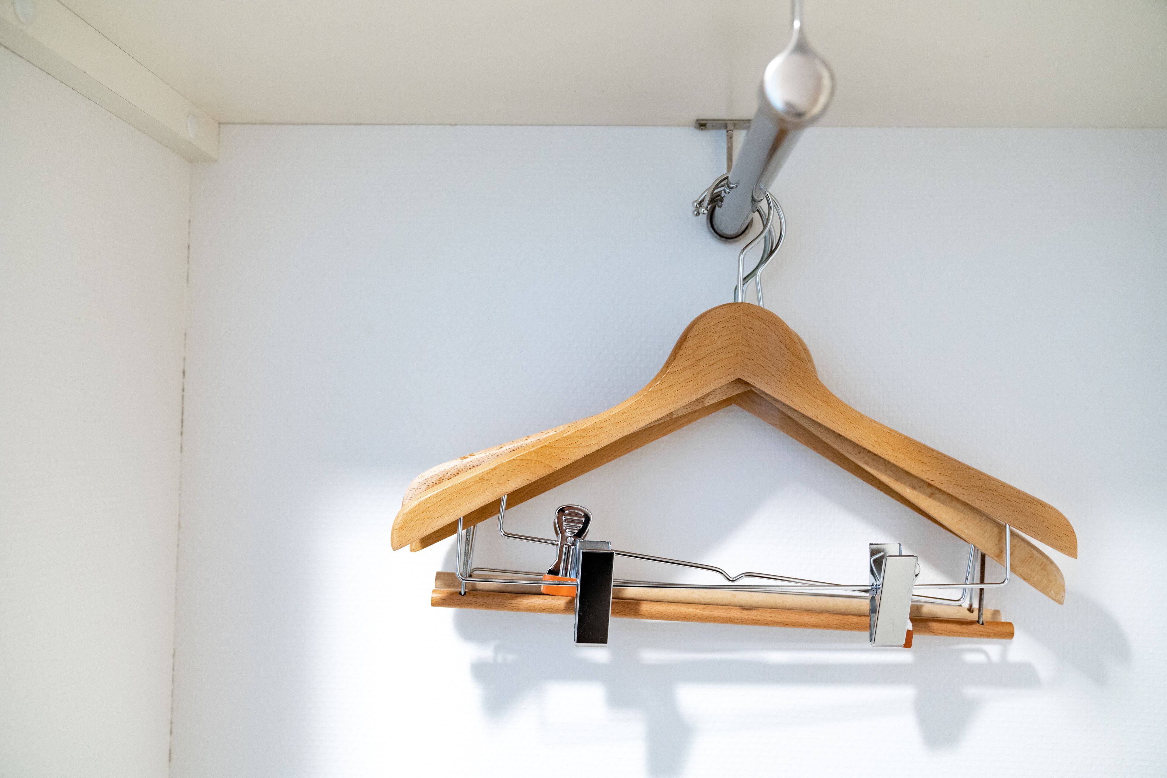 A wooden hanger with a metal clip, suspended from a ceiling hook.