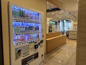 A vending machine with various beverage options and a wooden reception desk in the background. - The OneFive Fukuoka Tenjin (Fukuoka)