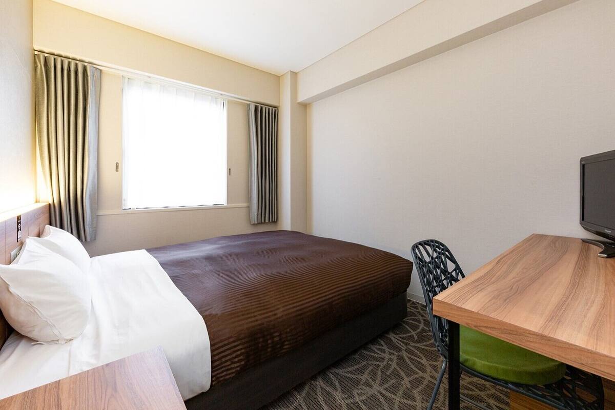 A hotel room with a bed, a desk with a television, and a chair.