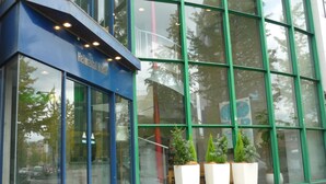 A modern hotel entrance with large glass windows, a blue awning, and potted plants on the sidewalk.